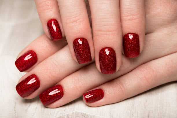 Red glittery nails on a wooden surface, showcasing a stylish manicure.