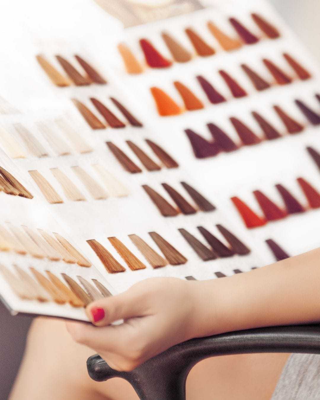 Person holding a hair color swatch book with various shades displayed.