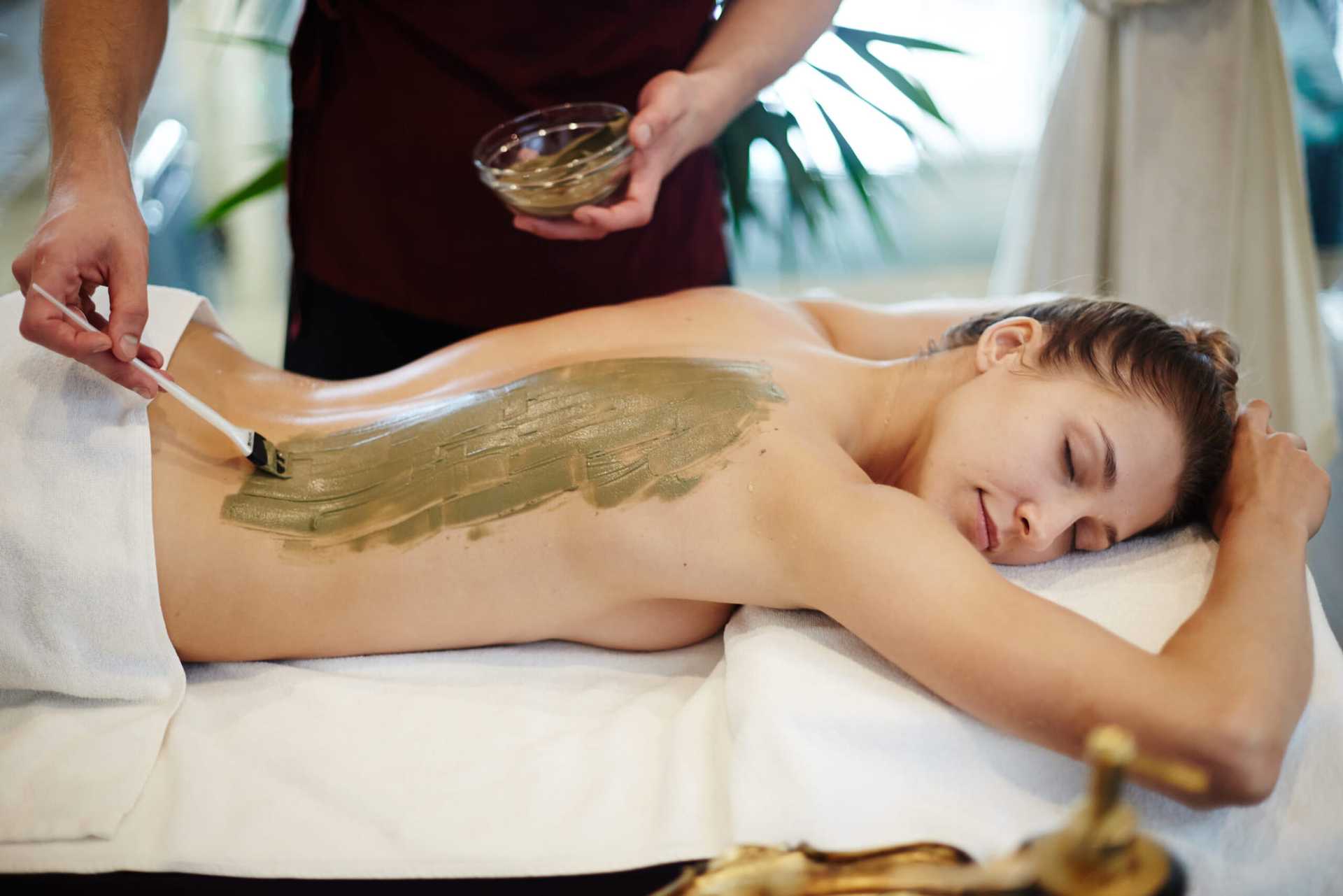 Person receiving a relaxing mud treatment on their back in a spa setting.