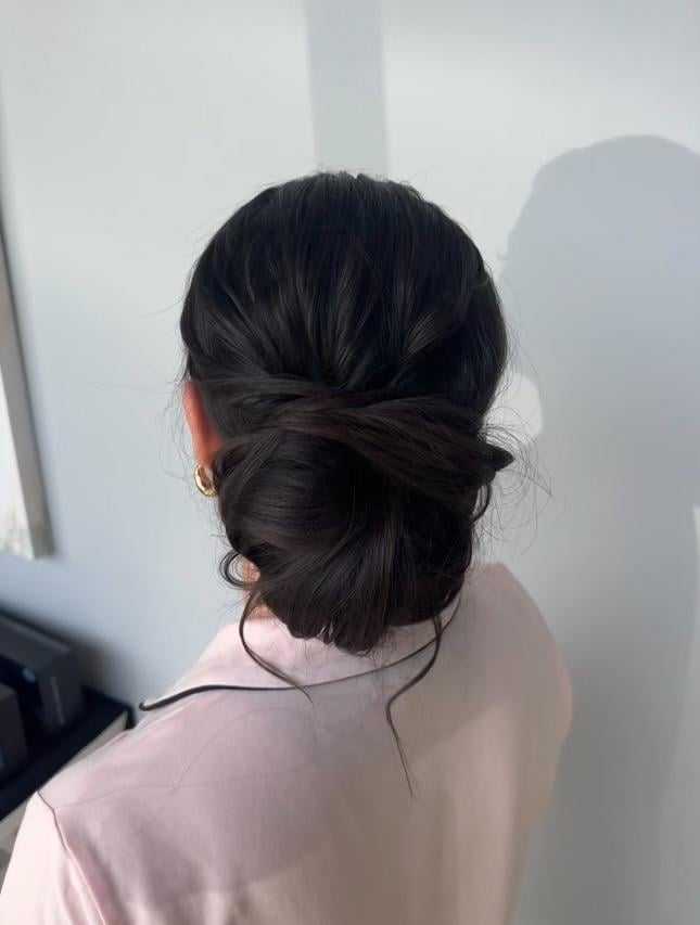Woman with dark hair in an elegant bun, wearing a light pink shirt, viewed from behind.