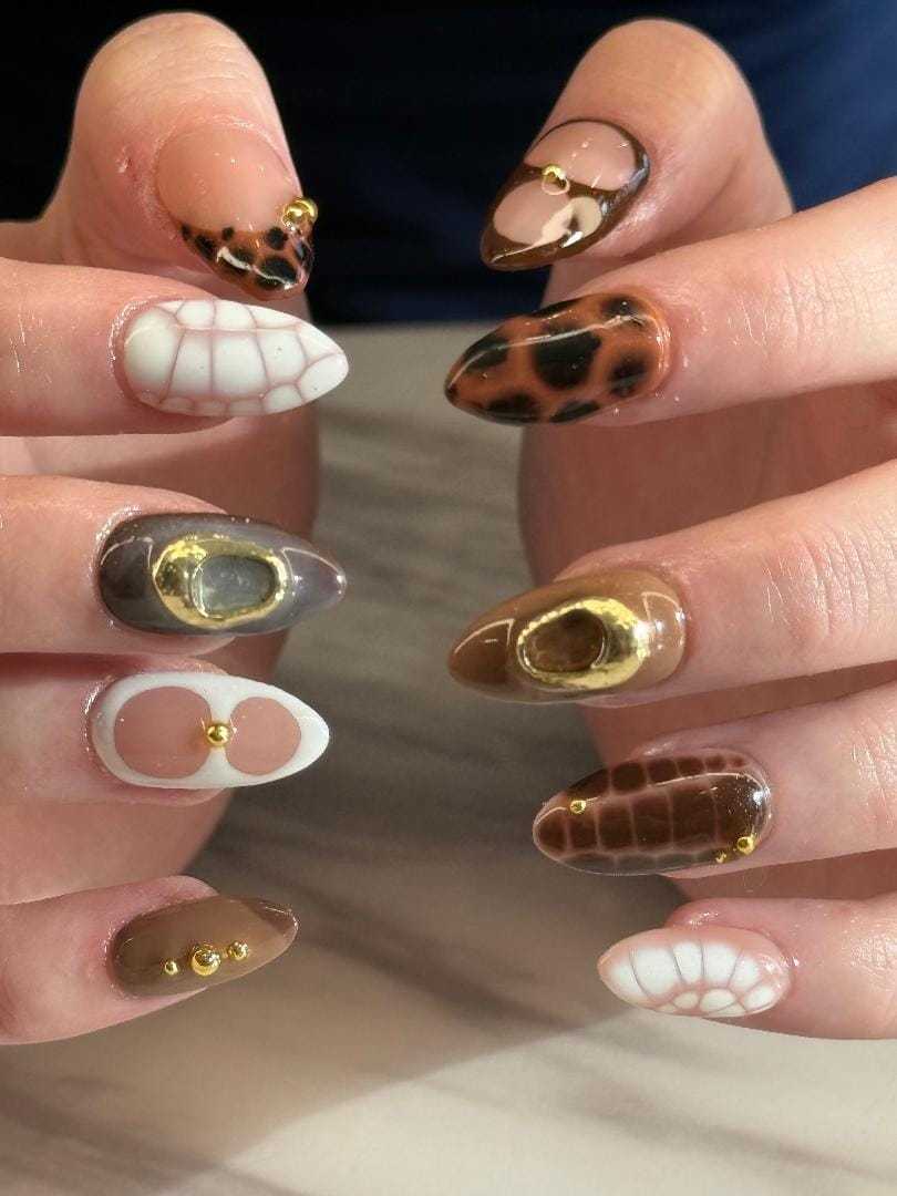 Stylish nails with geometric and animal print designs featuring gold accents.