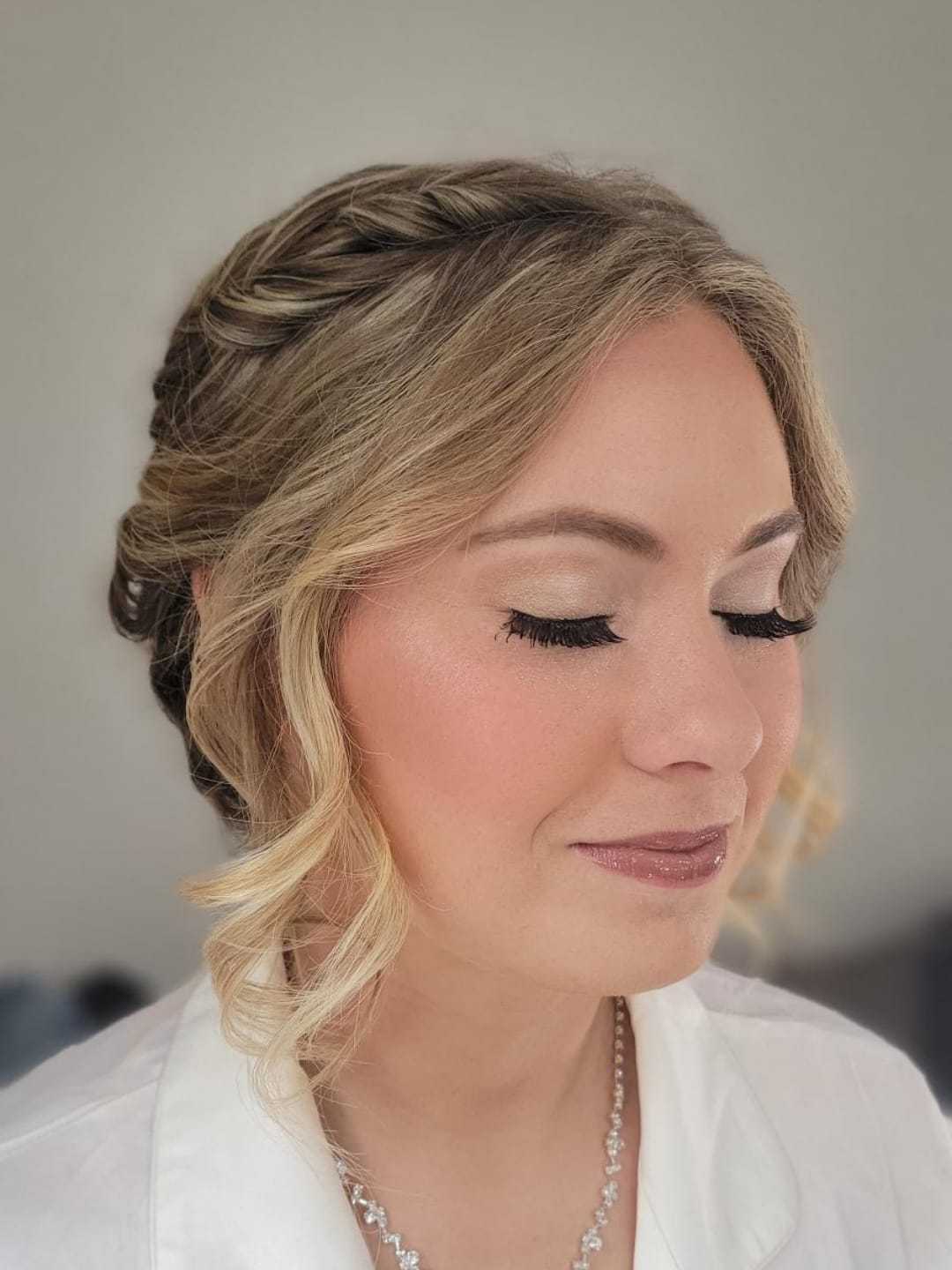 Woman with braided updo and soft makeup, eyes closed, wearing a white blouse.