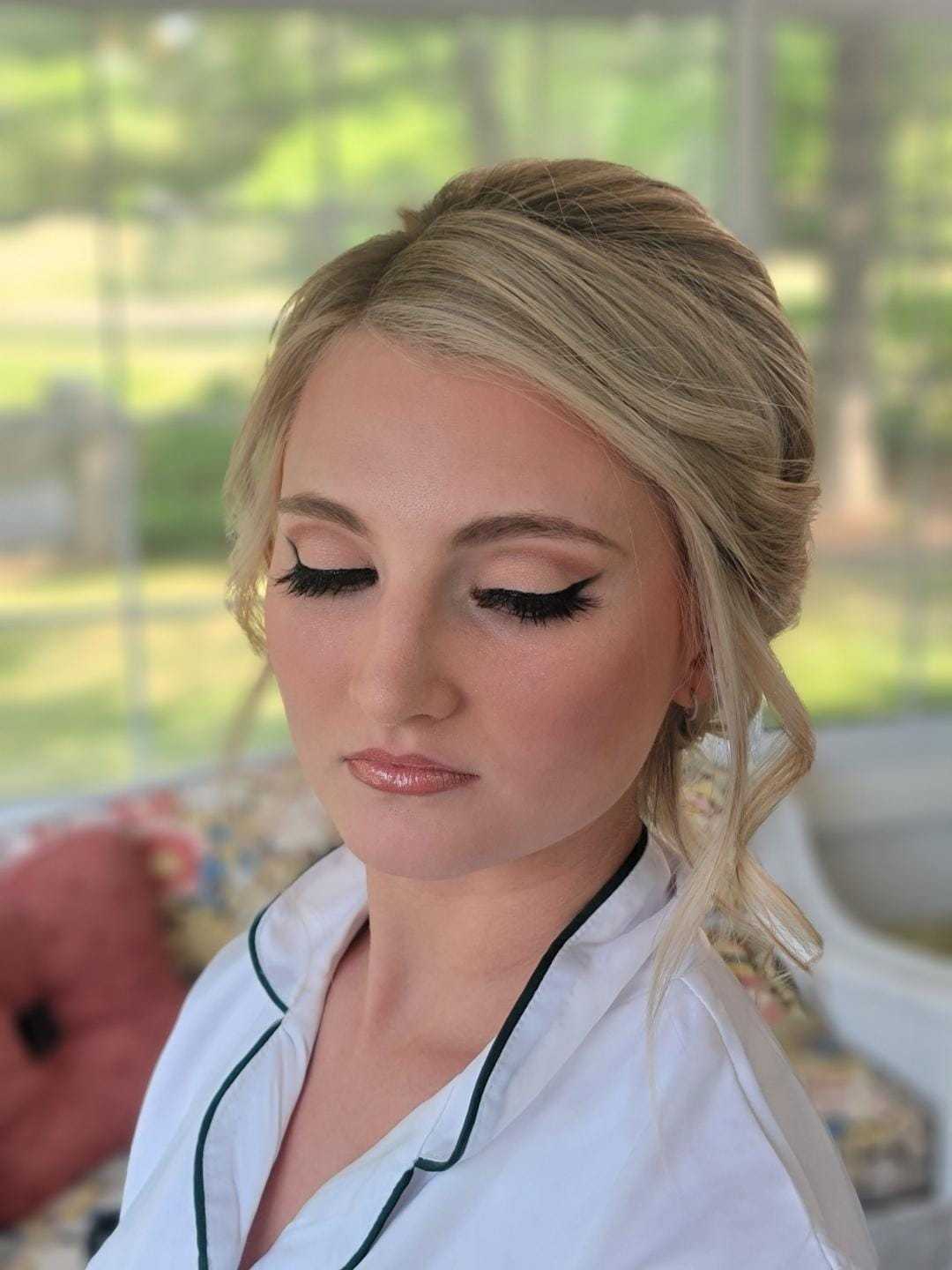 Young woman with elegant makeup and styled hair, wearing a white outfit, with eyes closed.