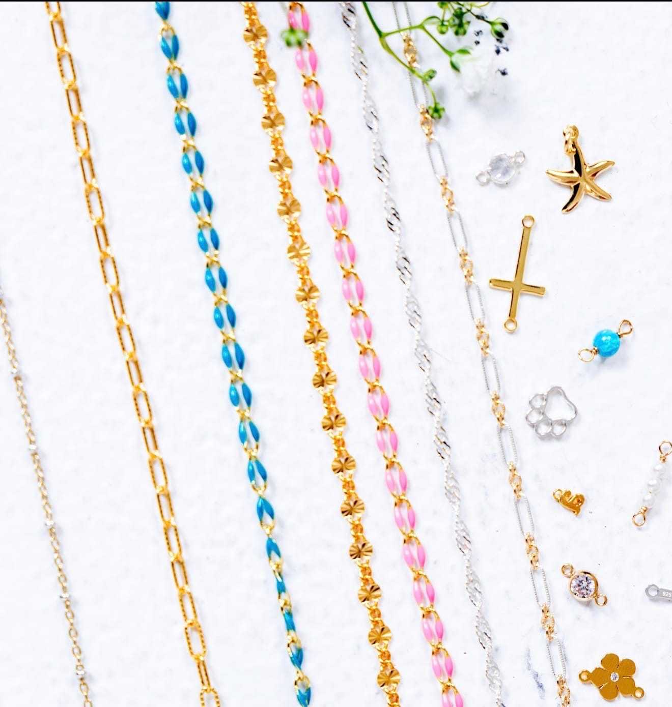 Gold and colorful chains with various charms on a white surface.