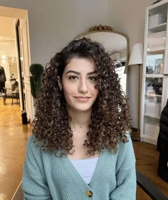 Woman with curly hair smiling in a cozy, modern living room setting.