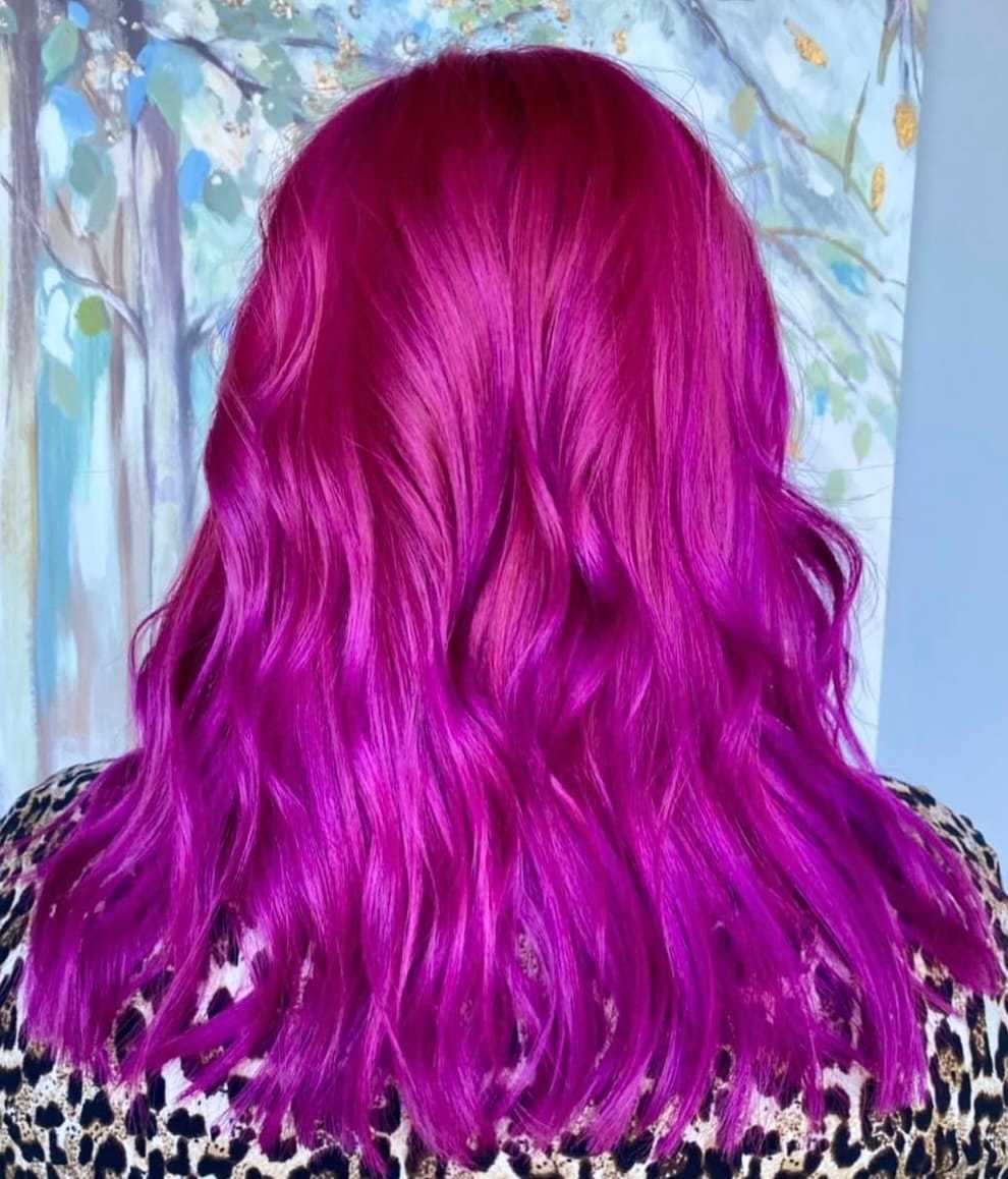 Vibrant magenta hair with soft waves against a blurred, colorful background.