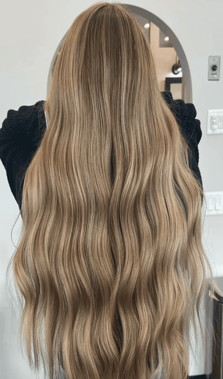Long wavy blonde hair flowing down the back of a person in a salon setting.