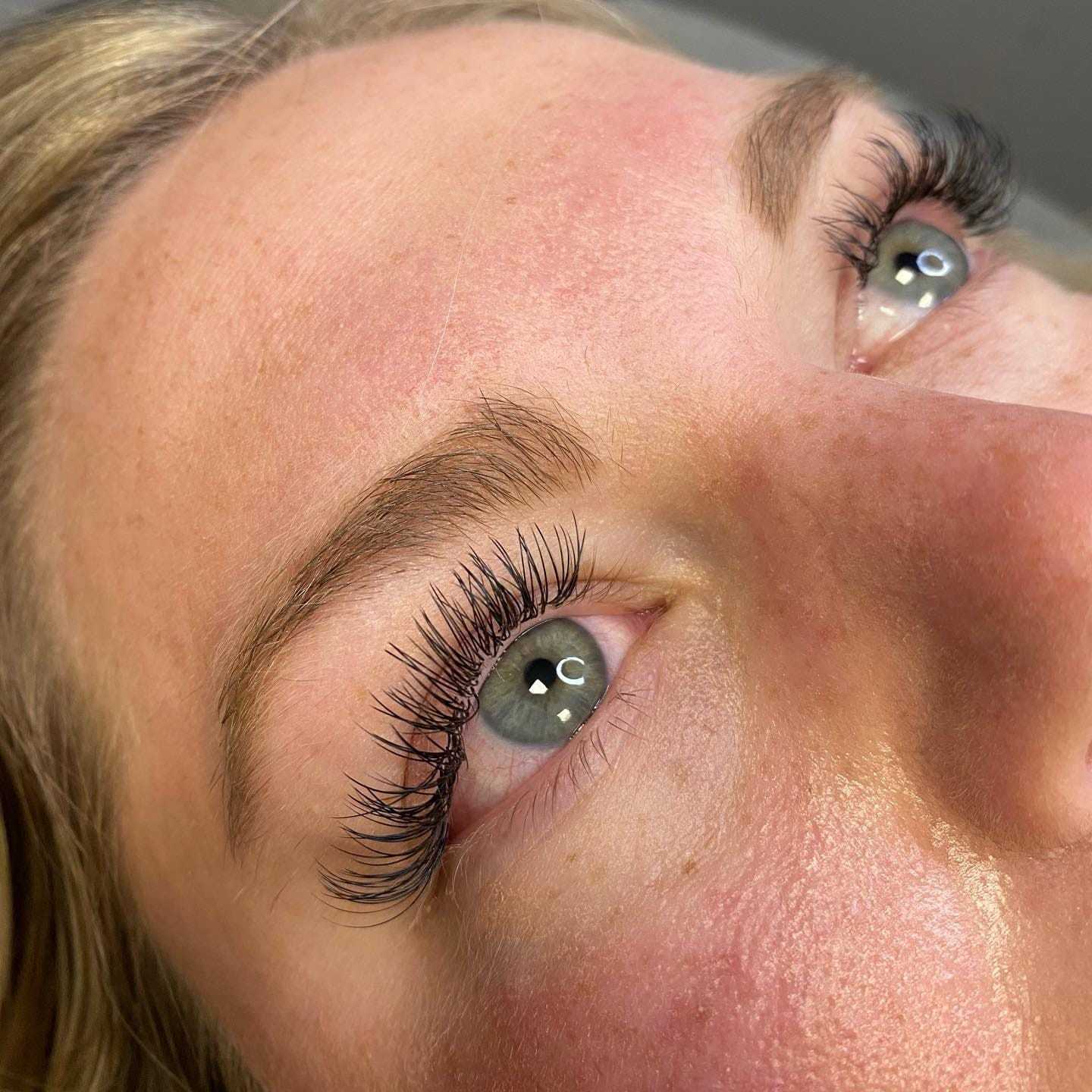 Close-up of a person with long, thick eyelashes and light blue eyes gazing upward.