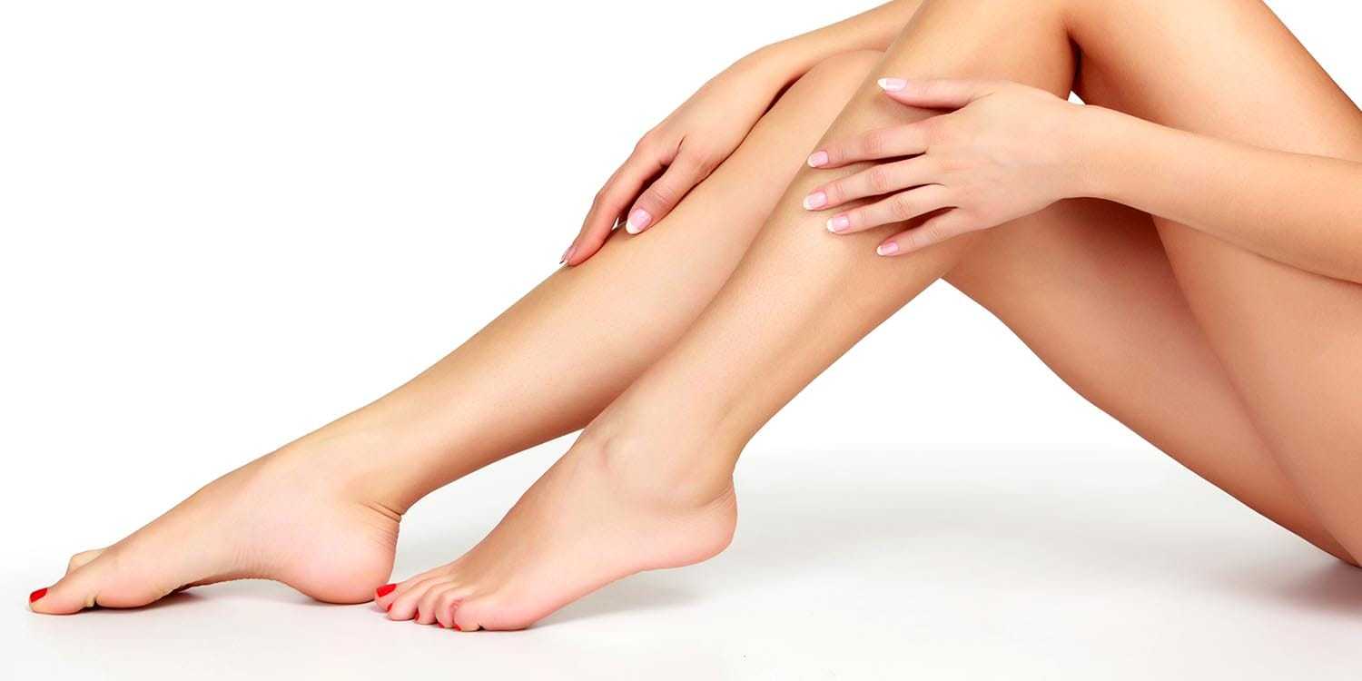 Smooth, hair-free female legs with red toenails, touching gently, isolated on white background.