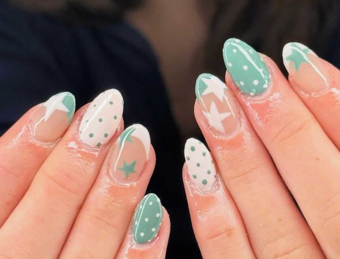 Green and white nail art with stars, polka dots, and negative space design.