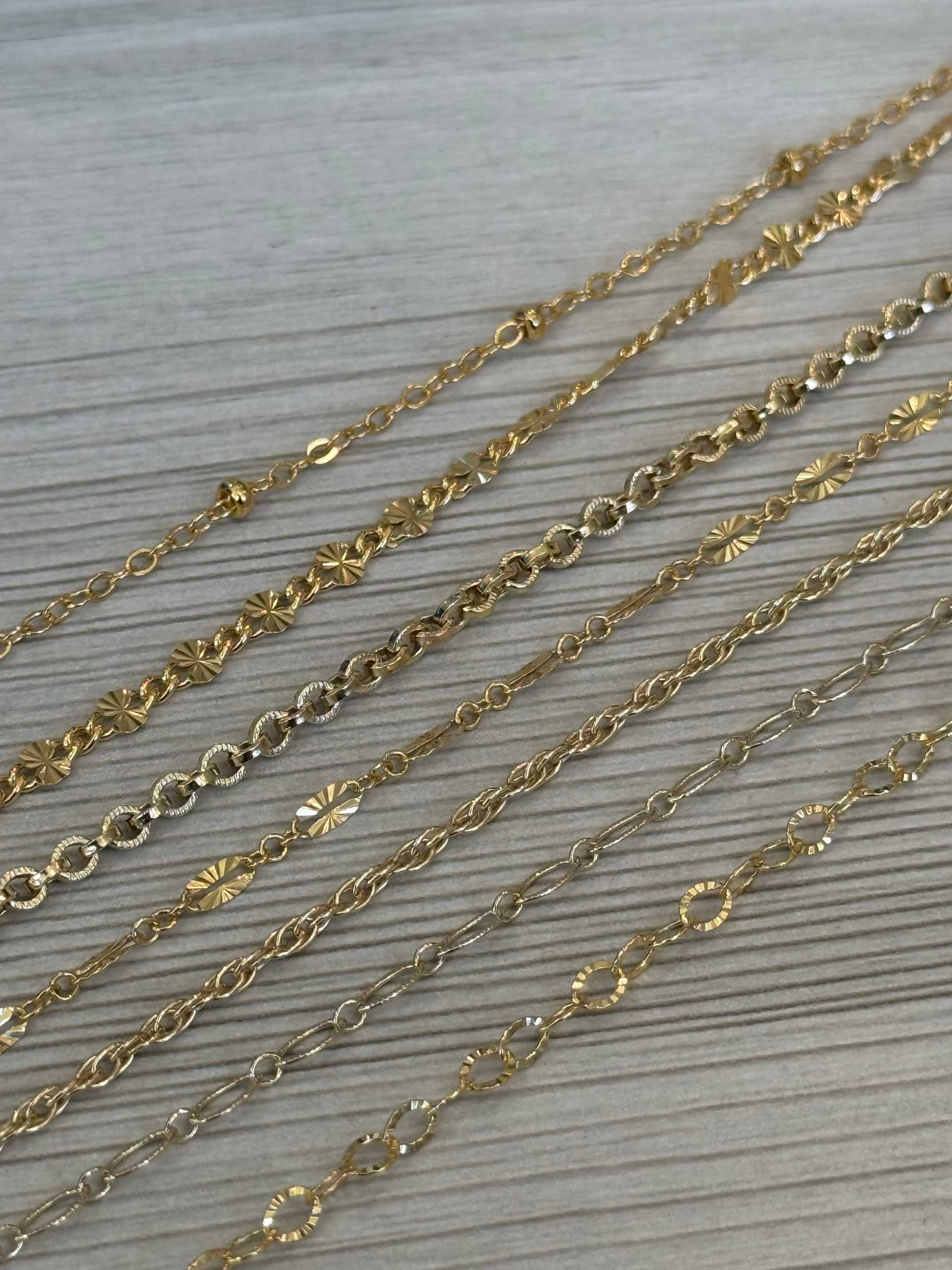Gold and silver chains with varied designs laid out on a wooden surface.