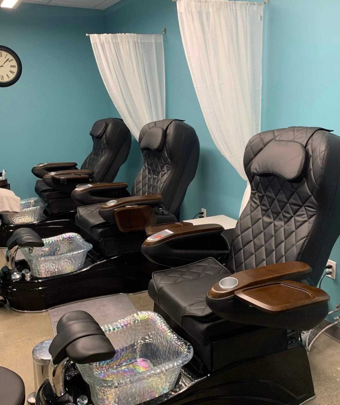 Four black massage chairs lined up in a spa with blue walls and white curtains in the background.