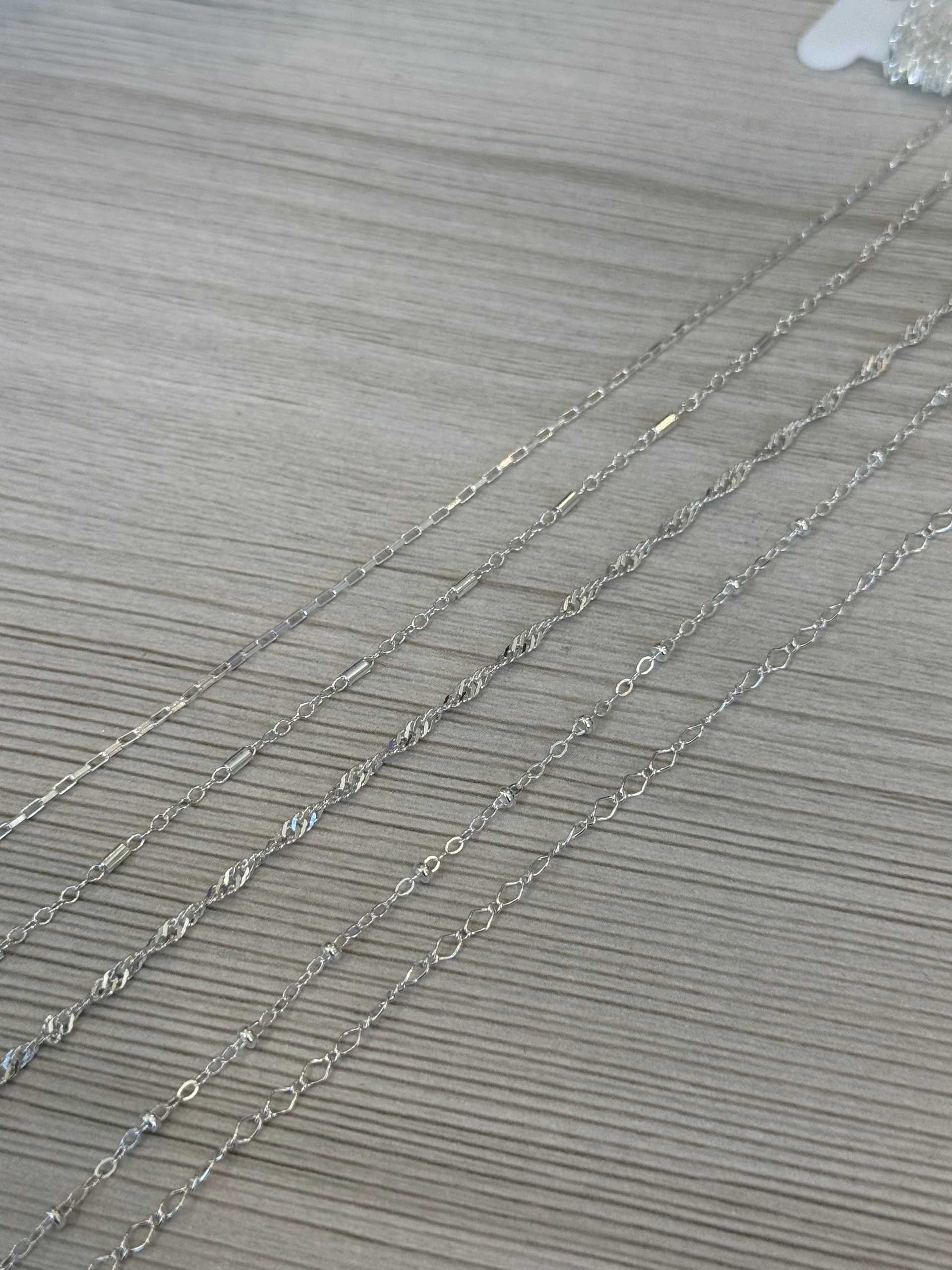 Silver chains displayed on a wooden surface.