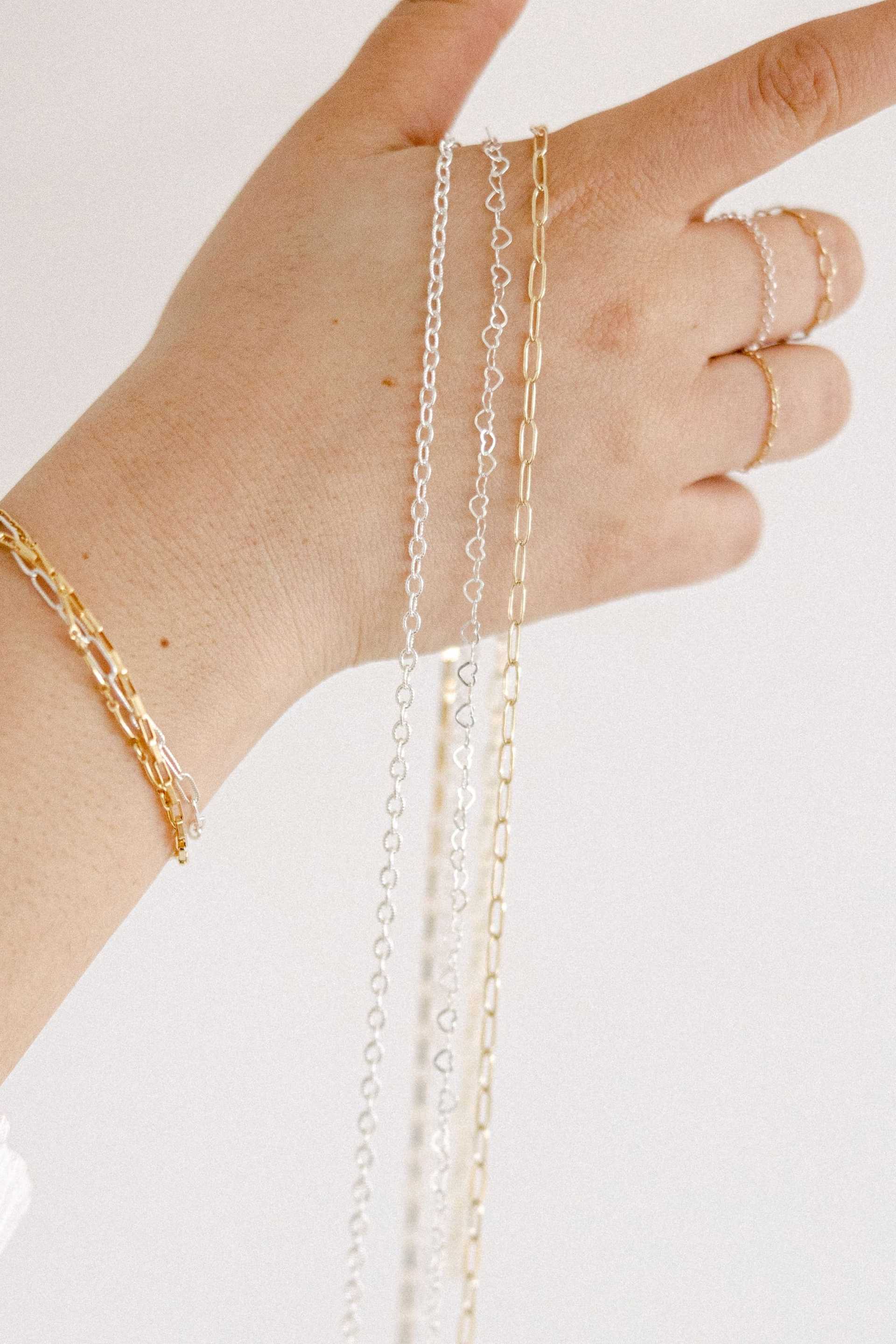 Hand displaying gold and silver chains and rings against a neutral background.