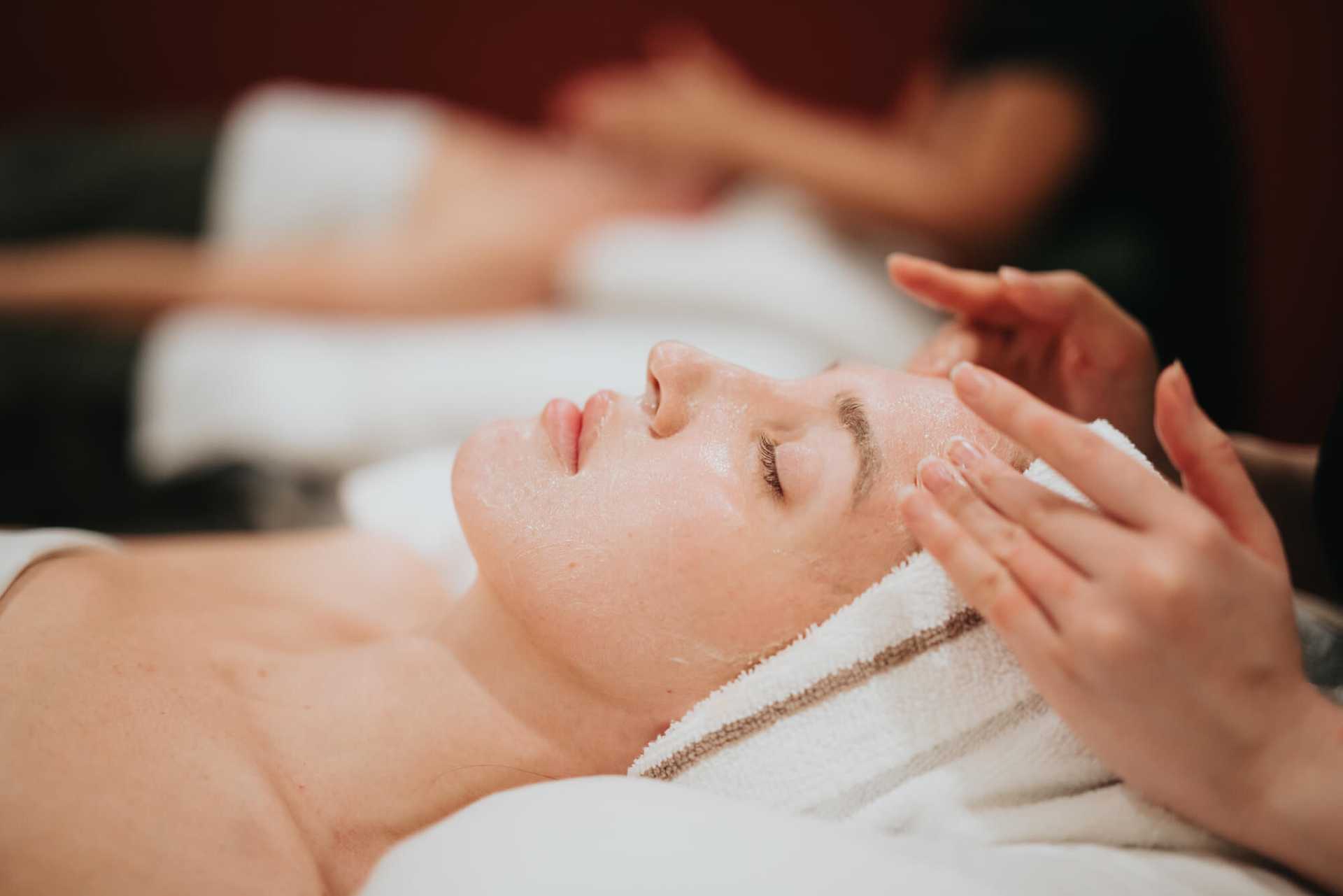 Person enjoying a relaxing facial massage at a spa, with a towel wrapped around their head.