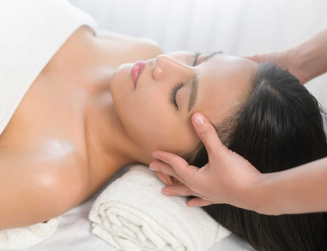 Person receiving a relaxing head massage at a spa, lying with eyes closed on a towel.