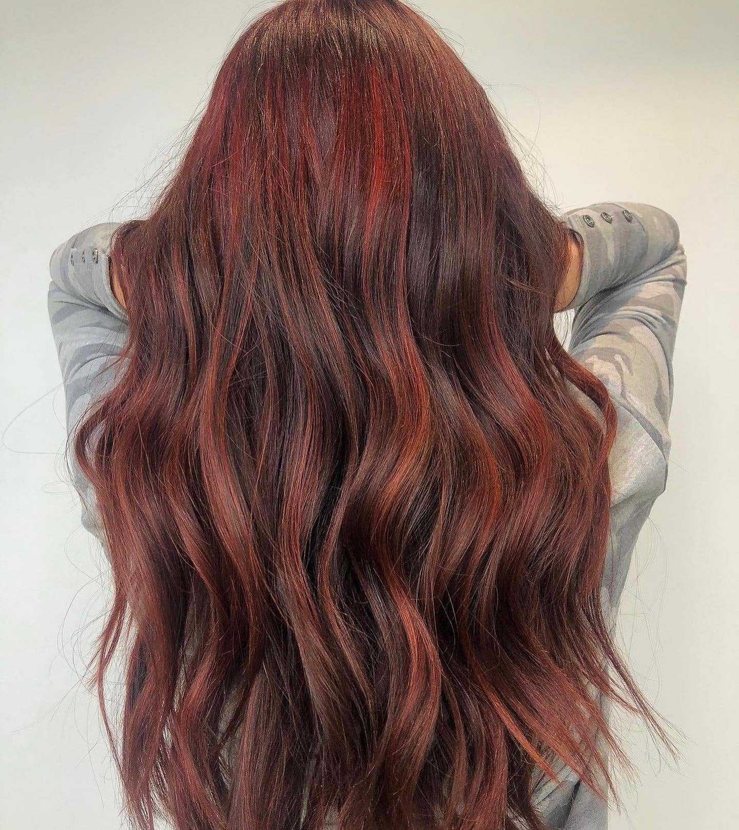 Long, wavy, rich auburn hair from the back against a neutral background.
