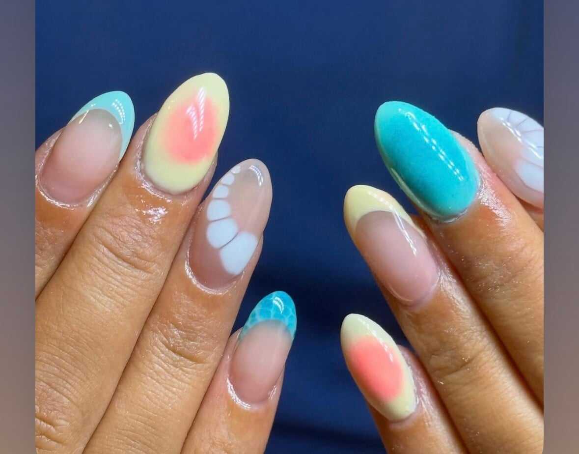 Colorful gel nail art with blue, yellow, pink designs and patterns on manicured hands.