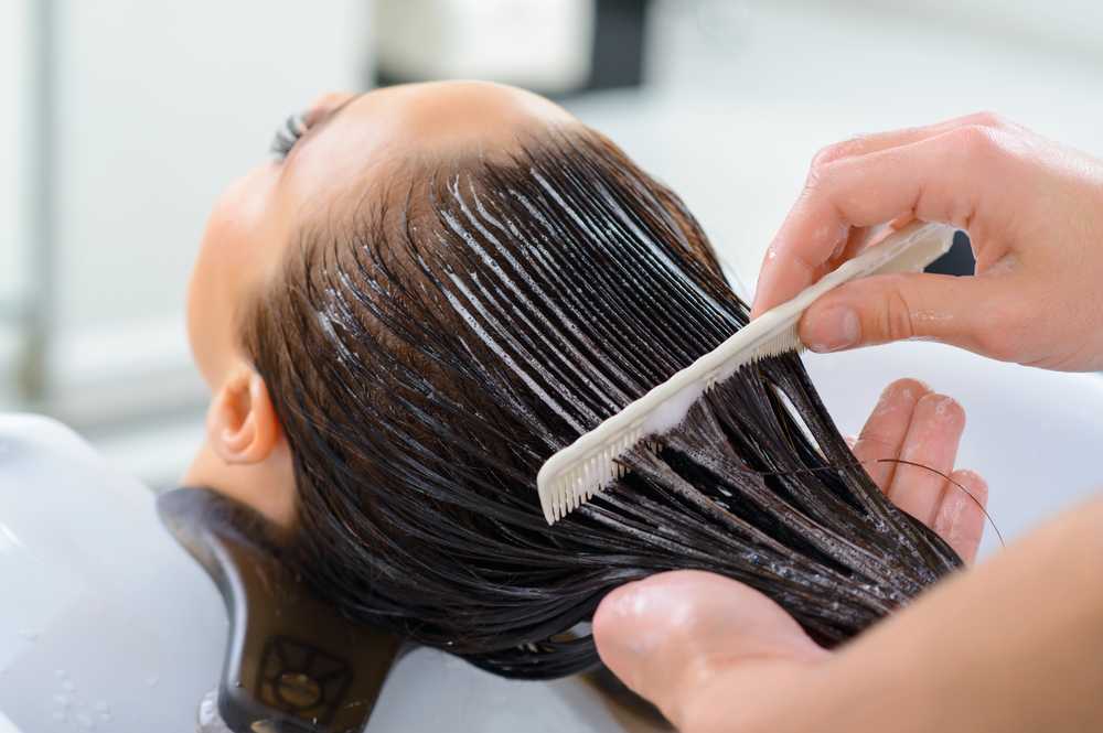 Hairdresser applying product to wet hair in a salon sink.