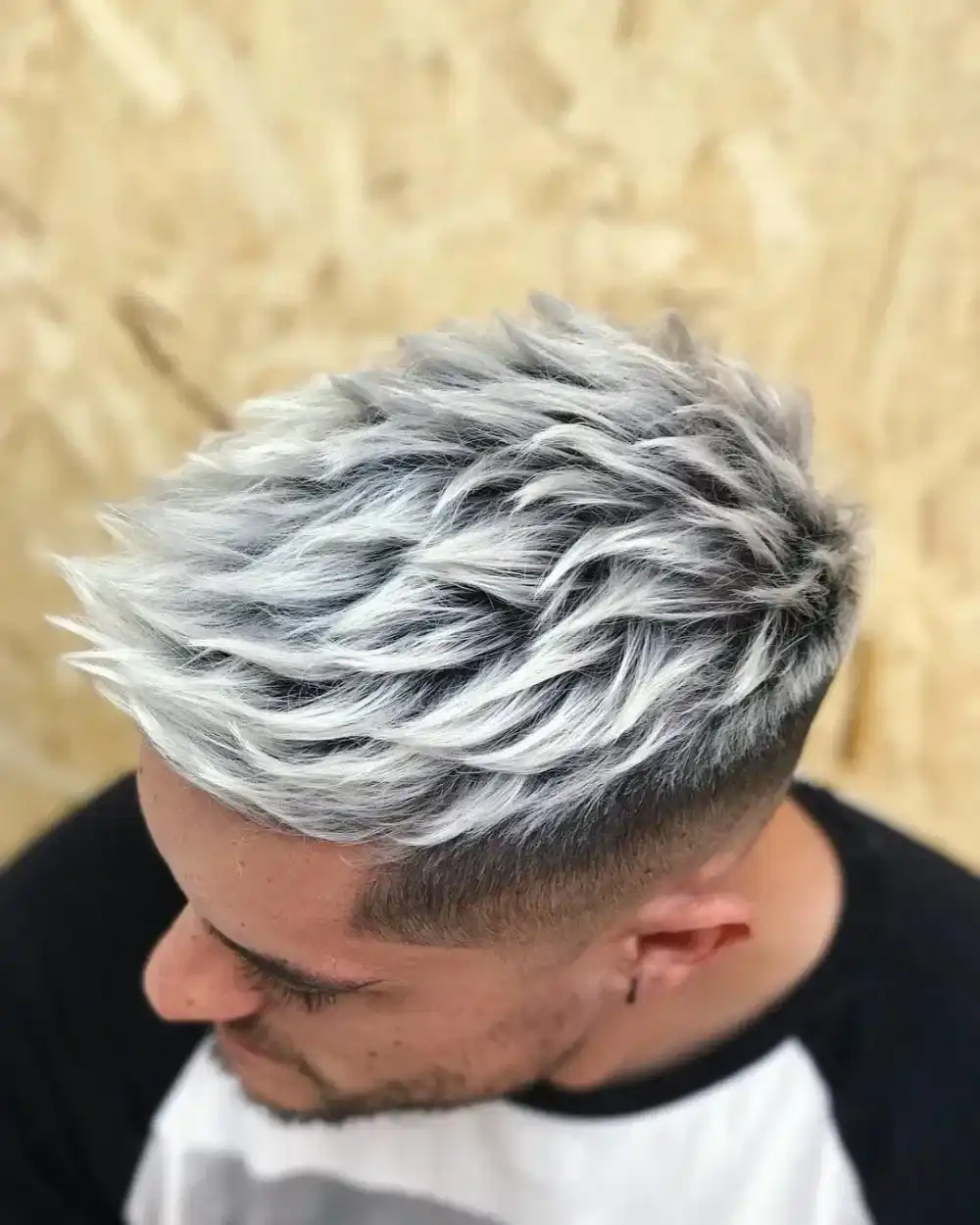 Man with short, textured, silver hair against a wooden background.