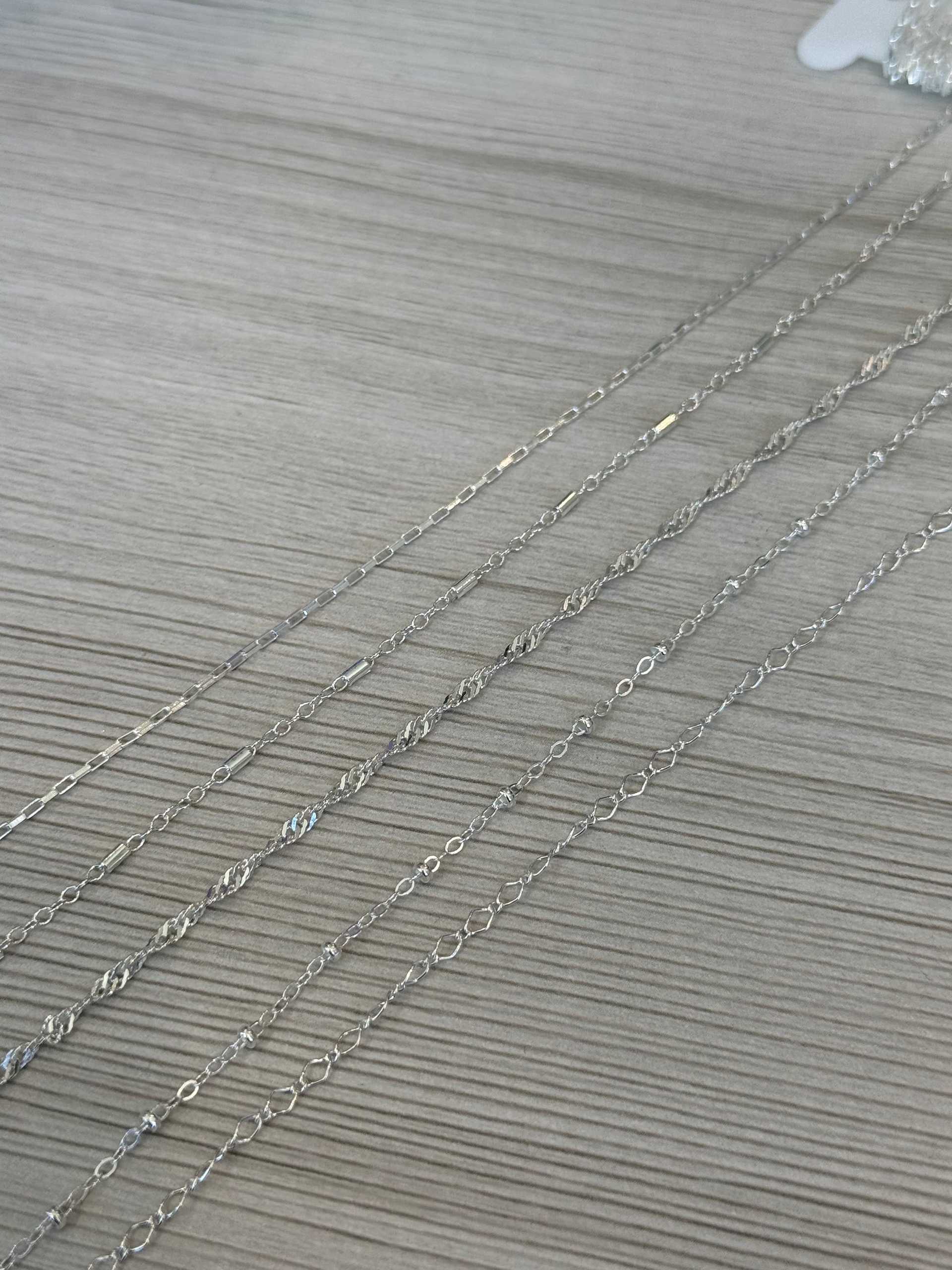 Silver chains displayed on a wooden surface.