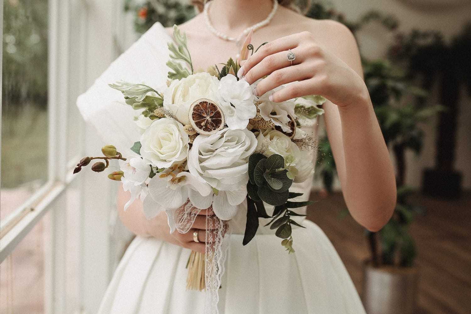 Bride holding elegant bouquet with white flowers and dried citrus accents.