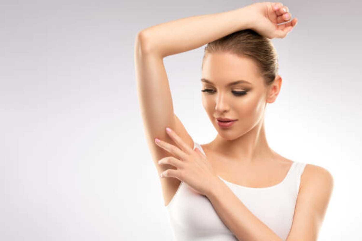 Woman in white tank top shows smooth underarm, highlighting skincare.