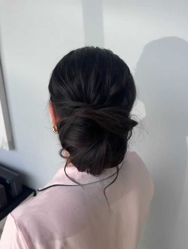 Woman with dark hair in an elegant bun, wearing a light pink shirt, viewed from behind.